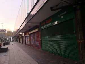 Image of green shutters closed beneath Orange Percy Ingle logo next to closed shutters of other shops.