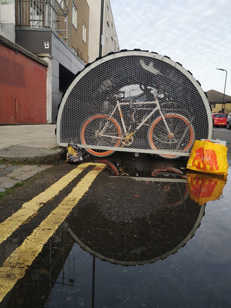 Bike in hangar reflected in puddle with Sainsbury's Elephant bag