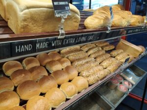 Loaves of bread and rolls laid out on racks. Between racks a sign reads 'HAND MADE WITH EXTRA LOVING CARE'
